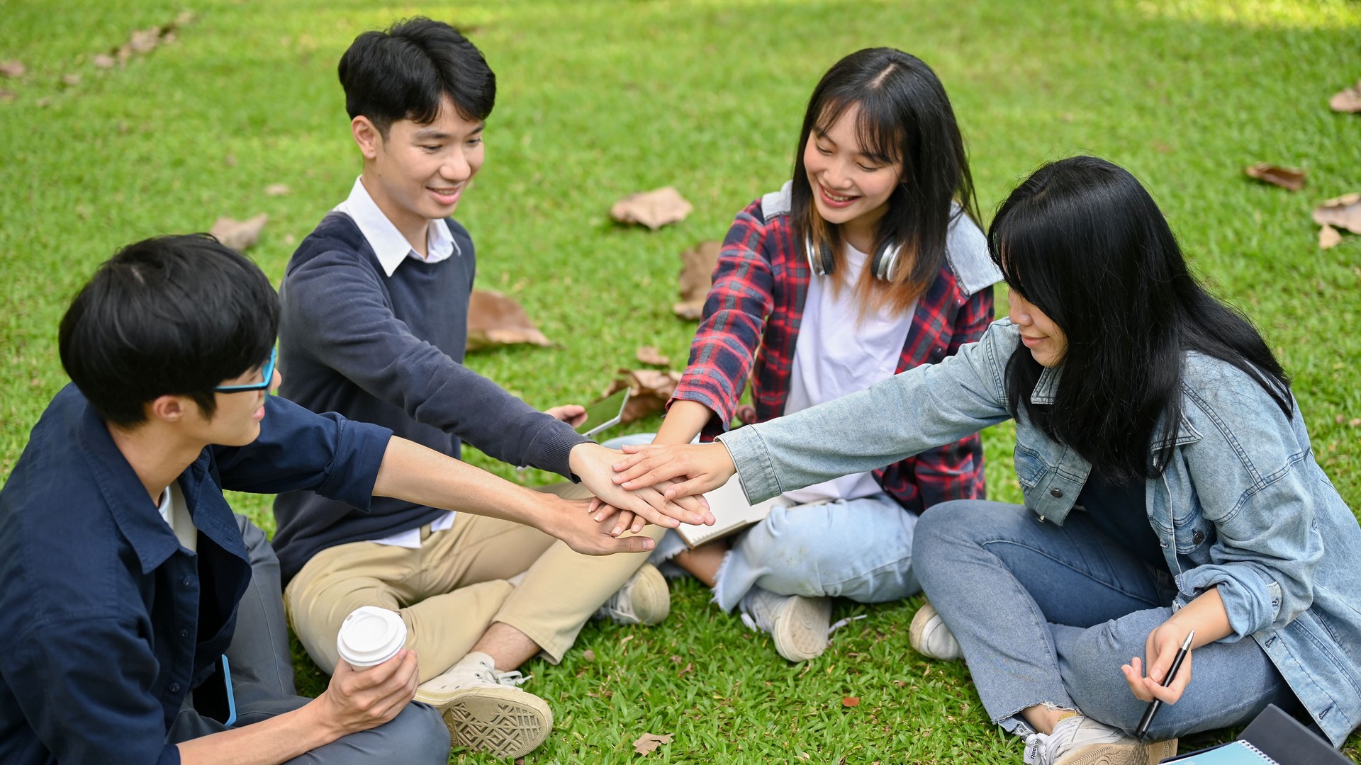 A group of Asian college students sitting in the park, putting their hands together, cheering up.
